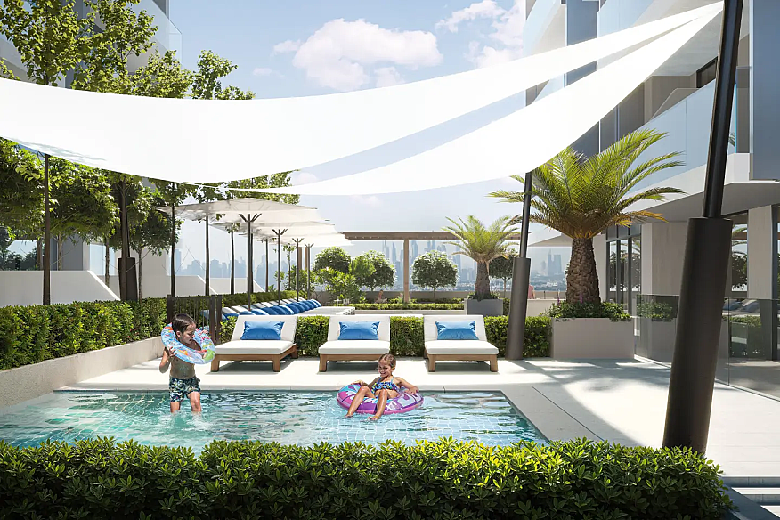 Открытая зона с бассейном, где дети играют, и шезлонги окружены зеленью.