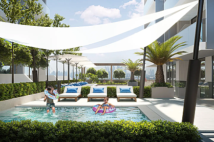 Открытая зона с бассейном, где дети играют, и шезлонги окружены зеленью.